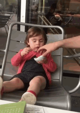 a little girl is sitting on a chair eating a bowl of food .