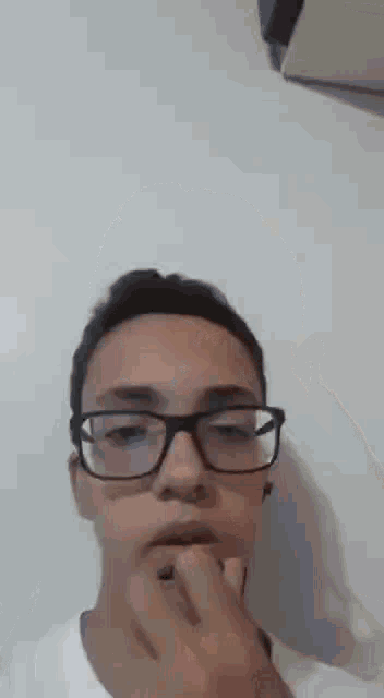 a young man wearing glasses and a white shirt is making a face .