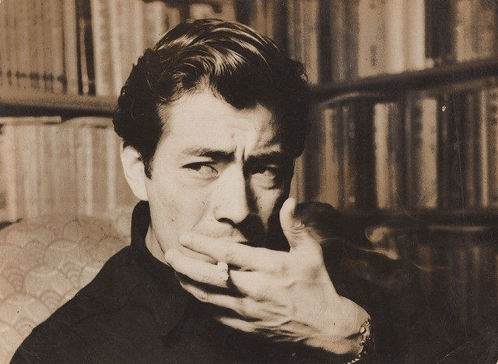 a man is covering his mouth with his hand in front of a bookshelf