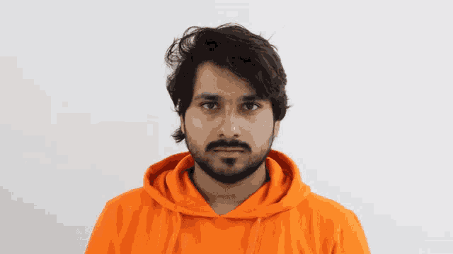 a man with a beard wearing an orange hoodie makes a funny face