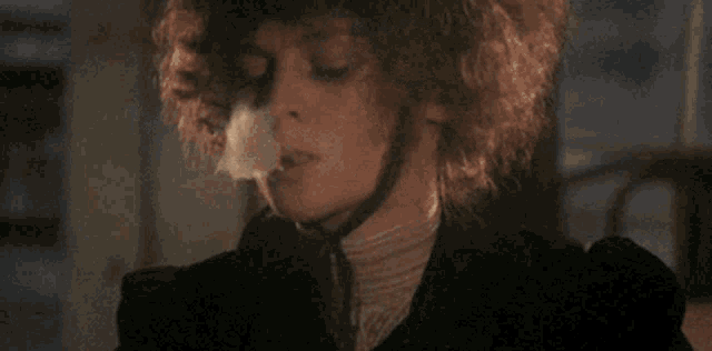 a woman with curly hair is smoking a cigarette and making a cloud of smoke coming out of her mouth .