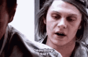 a man with long hair is talking to another man while looking at the camera .