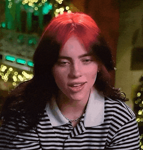 billie eilish is wearing a striped shirt and a necklace and has red hair .