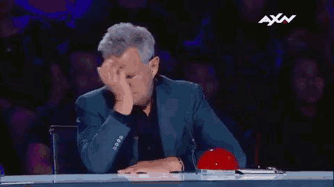 a man in a blue suit is sitting at a table with his hand on his forehead .