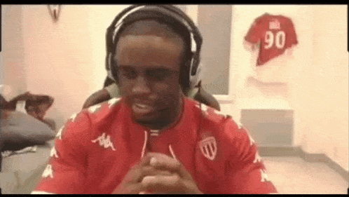 a man wearing headphones and a red shirt is sitting in a room with a jersey on the wall .
