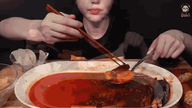 a person is eating a large plate of food with chopsticks and a spoon