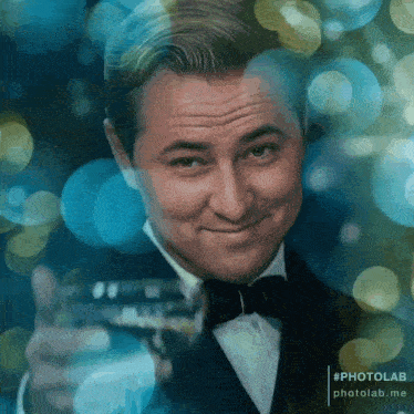 a man in a tuxedo and bow tie holds a glass of wine