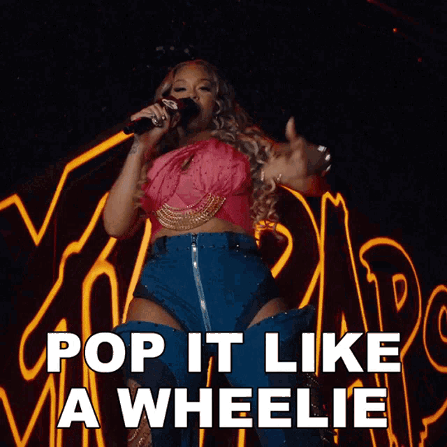 a woman singing into a microphone with the words pop it like a wheelie behind her