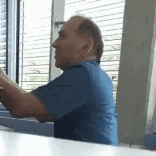 a man in a blue scrub top is sitting in front of a window