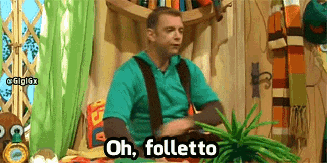 a man in a green shirt and suspenders is sitting at a table and says oh folletto .