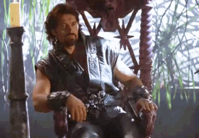 a man in a leather vest is sitting in a chair