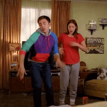 a man and a woman are dancing in a living room with a picture of a mountain on the wall