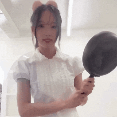 a woman in a white shirt is holding a frying pan in her hand