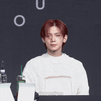 a young man with red hair is sitting at a table with a cup of coffee and a bottle of water
