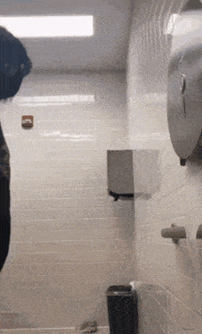 a toilet with a paper towel dispenser and a black trash can