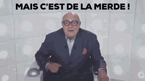a man in a suit and glasses is sitting in front of a white wall with the words mais c 'est de la merde !