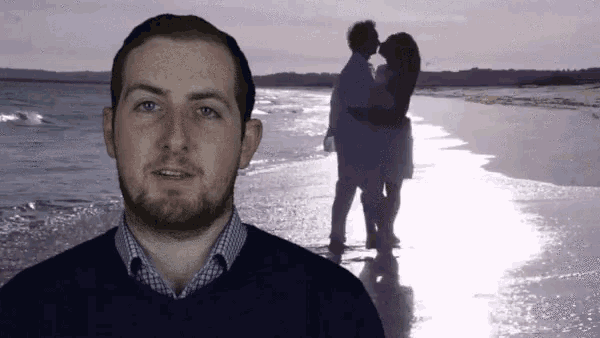 a man stands in front of a silhouette of a couple kissing on the beach