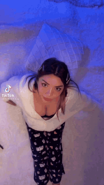 a woman in pajamas is standing on a bed with her arms outstretched and a blue light behind her .