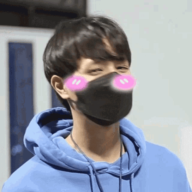 a young man wearing a blue hoodie and a black mask with pink eyes .