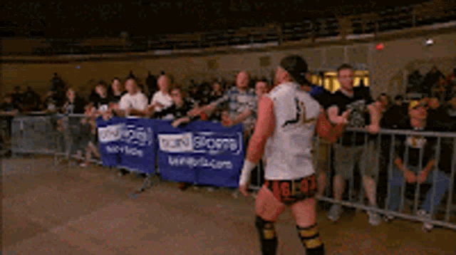 a wrestler is standing in front of a crowd in front of a banner that says icon sports