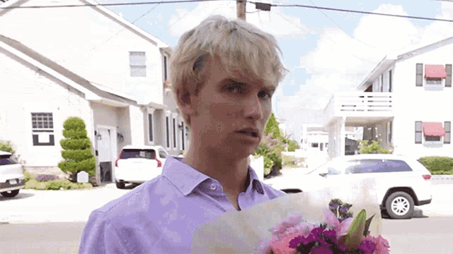 a man in a purple shirt holds a bouquet of pink flowers
