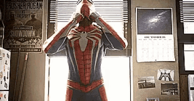 a man in a spiderman costume is standing in front of a window with his hands on his face .