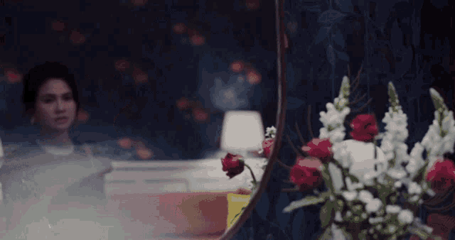 a woman looking at herself in a mirror with flowers in front of her