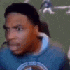 a man in a blue sweatshirt is sitting in a chair making a funny face .