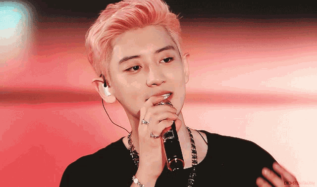 a man with pink hair sings into a microphone