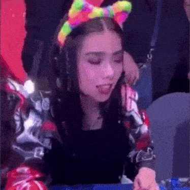 a woman wearing a rainbow colored headband is sitting in a crowd .