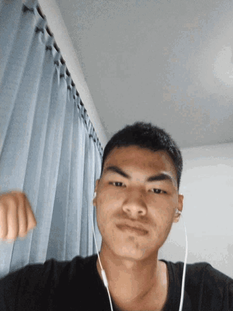 a young man wearing ear buds is standing in front of a blue curtain