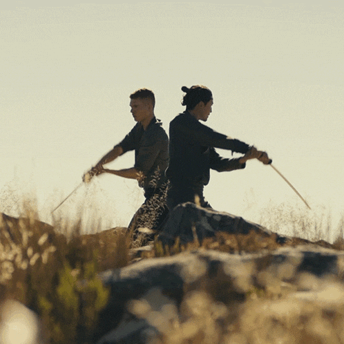 two men are standing back to back holding swords