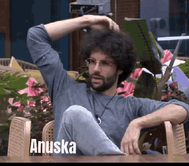 a man with curly hair and glasses is sitting in a chair with the name anuska written on the bottom