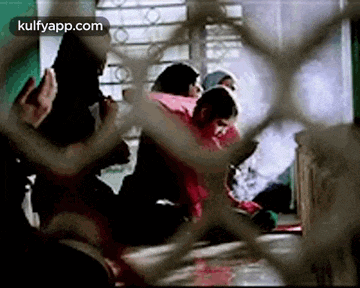 a group of people are sitting on the floor behind a fence in a room .