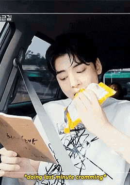 a man in a car reading a book and eating a snack