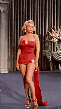 a woman in a red dress and heels is standing in front of a curtain in a room .