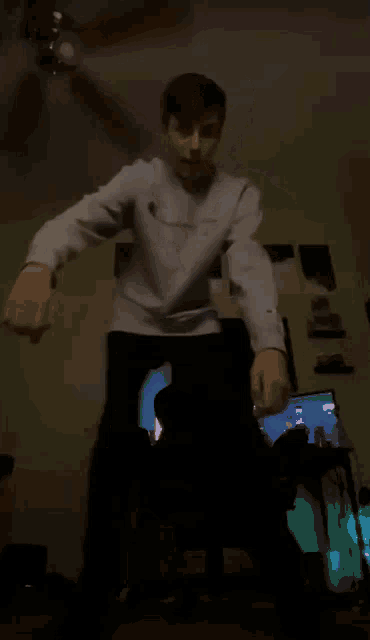 a person is dancing in a dark room with a ceiling fan in the background