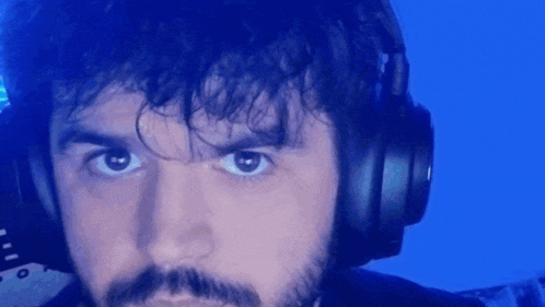 a man with a beard is wearing headphones and looking at the camera with a blue background .