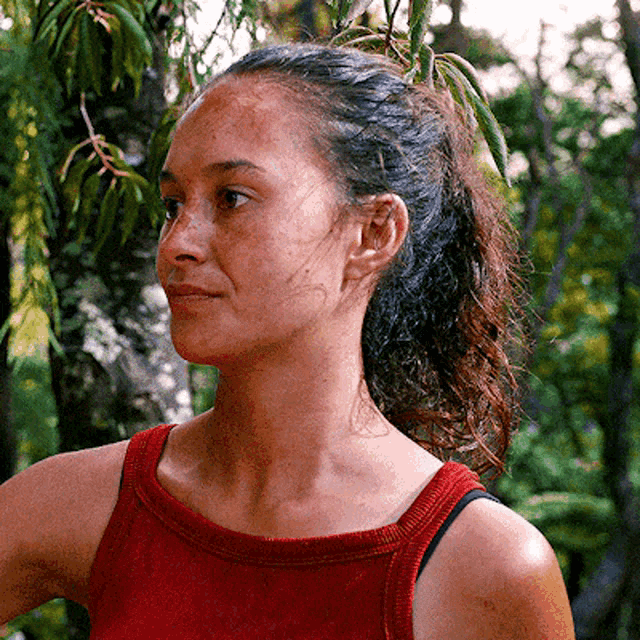 a woman wearing a red tank top is standing in the woods