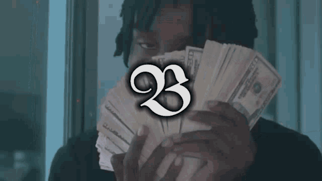 a man is holding a stack of money with the number 23 on the bottom