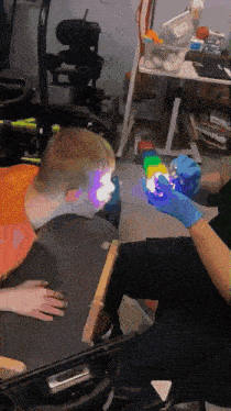 a person wearing blue gloves holds a cube in front of a child in a wheelchair