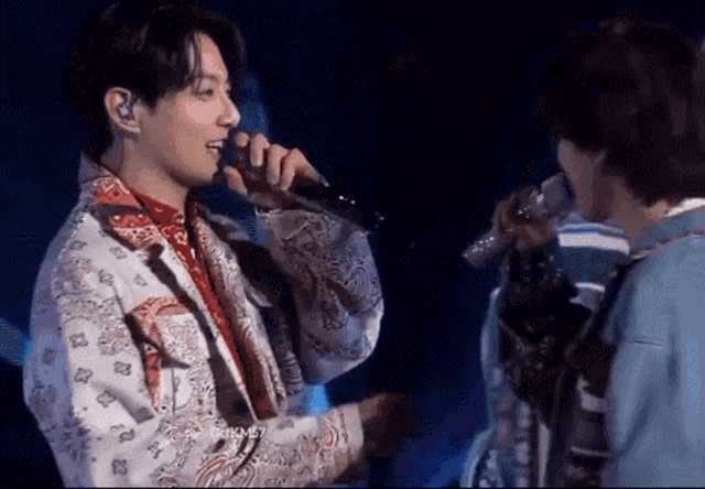 a man in a bandana is singing into a microphone while another man looks on .