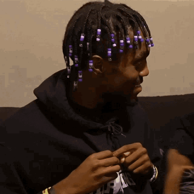 a man with purple beads in his hair is wearing a black hoodie with the letter r on the front