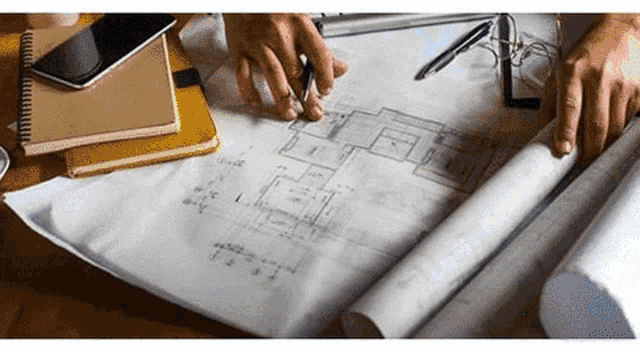 a person is sitting at a table looking at a blueprint of a house .
