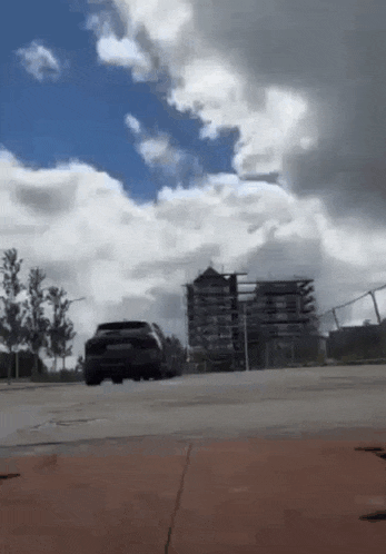 a car is driving down a street in a parking lot with a cloudy sky in the background .