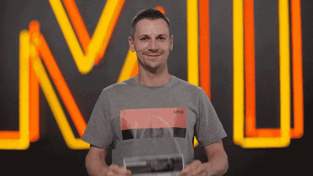 a man wearing a grey mini t-shirt is holding a trophy