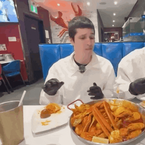 a man wearing black gloves is eating crab legs
