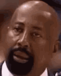 a bald man with a beard is looking at the camera with his mouth open .