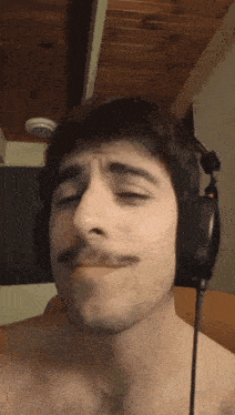 a shirtless man with a mustache is wearing headphones and making a funny face