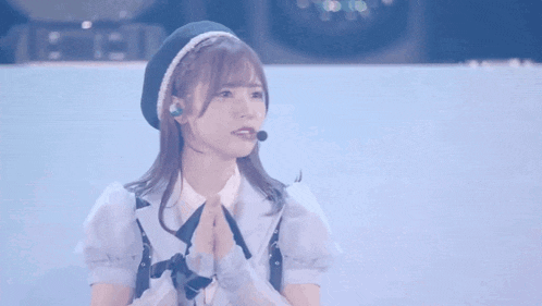a girl wearing a beret and a microphone is standing on a stage with her hands together .